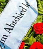 Rote Rosen mit Wassertropfen und einem weißen Band mit der Aufschrift „Zum Abschied“ auf grünem Hintergrund.